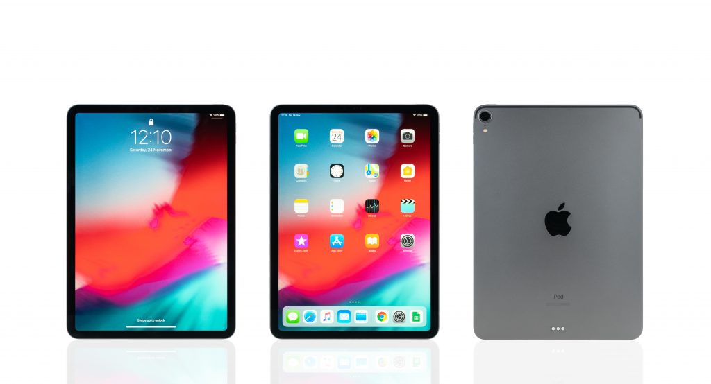 Studio shot of the space gray-colored Apple iPad, displaying the home and lock screen and rear view logo.